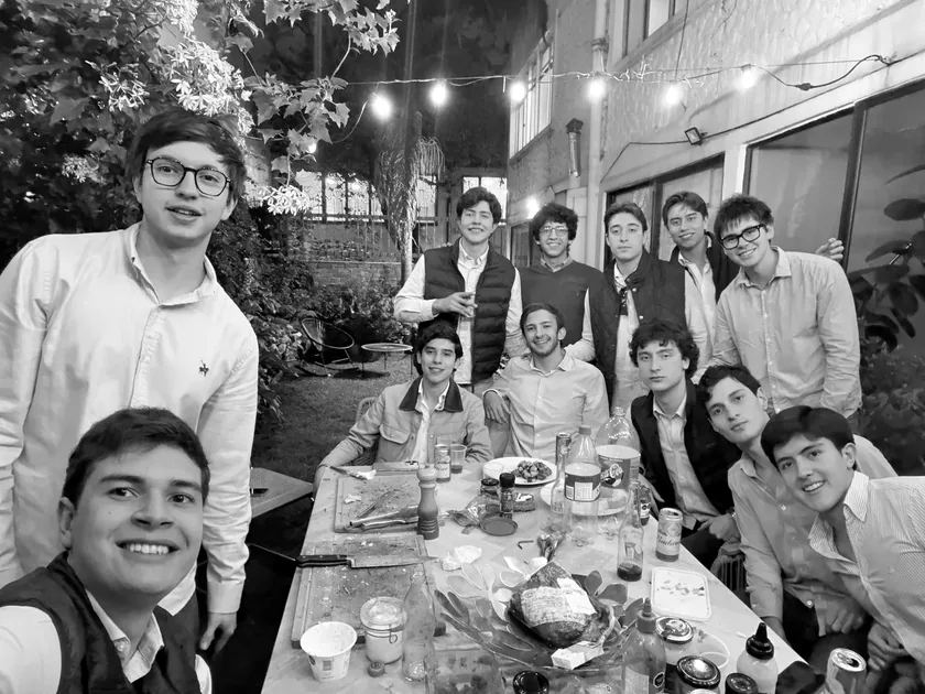 Juan Felipe con sus amigos en una comida larga, de noche, alrededor de una mesa.